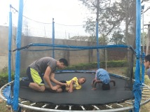 Caleb wrestling with James while Ami does somersaults on the trampoline.